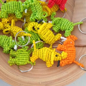 A wooden bowl filled with vibrant beaded keychains shaped like small animals, featuring dinosaur designs in green, yellow, and red colors.