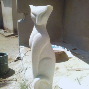 Tall and elegant white stone sculpture of a cat displayed outdoors, highlighting smooth curves and modern design in an artistic workspace.