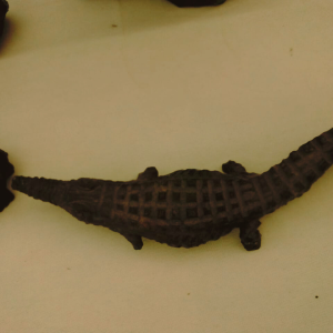 Dark crocodile-shaped object with patterned texture on back, set against a light background.