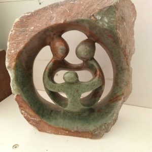A decorative stone sculpture featuring a circular design with two abstract figures embracing a smaller figure in the center. This portrays significant family bonds