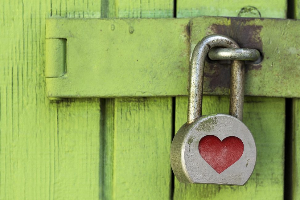 Close-up of a silver padlock featuring a red heart cutout, secured on a weathered green wooden door, symbolizing love and security.