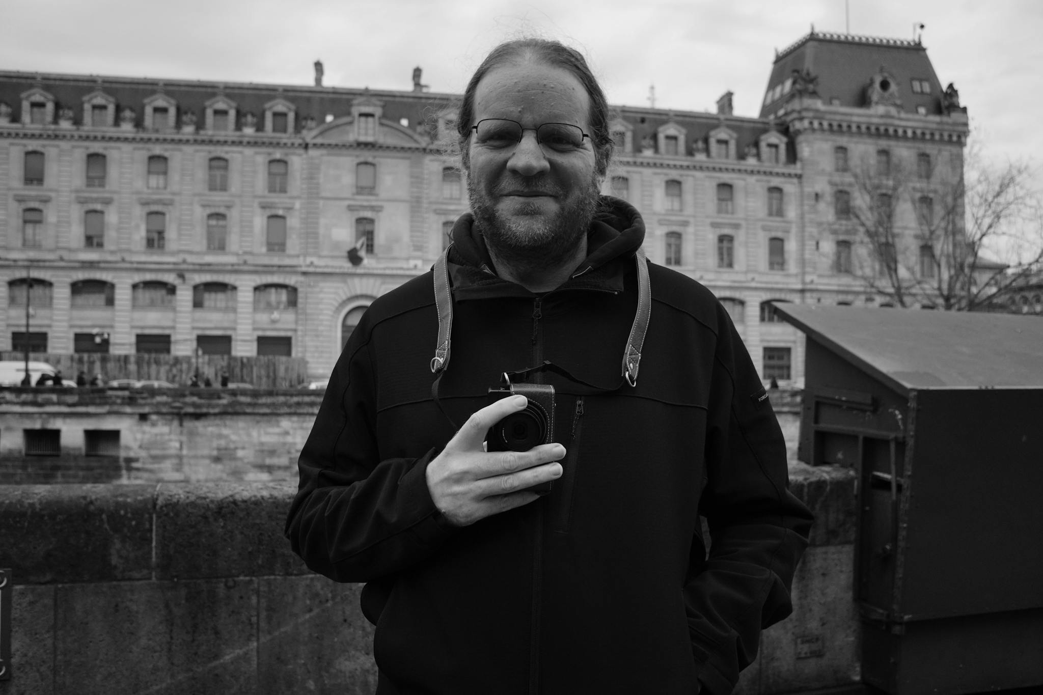 Man holding camera in urban setting with classic architecture.