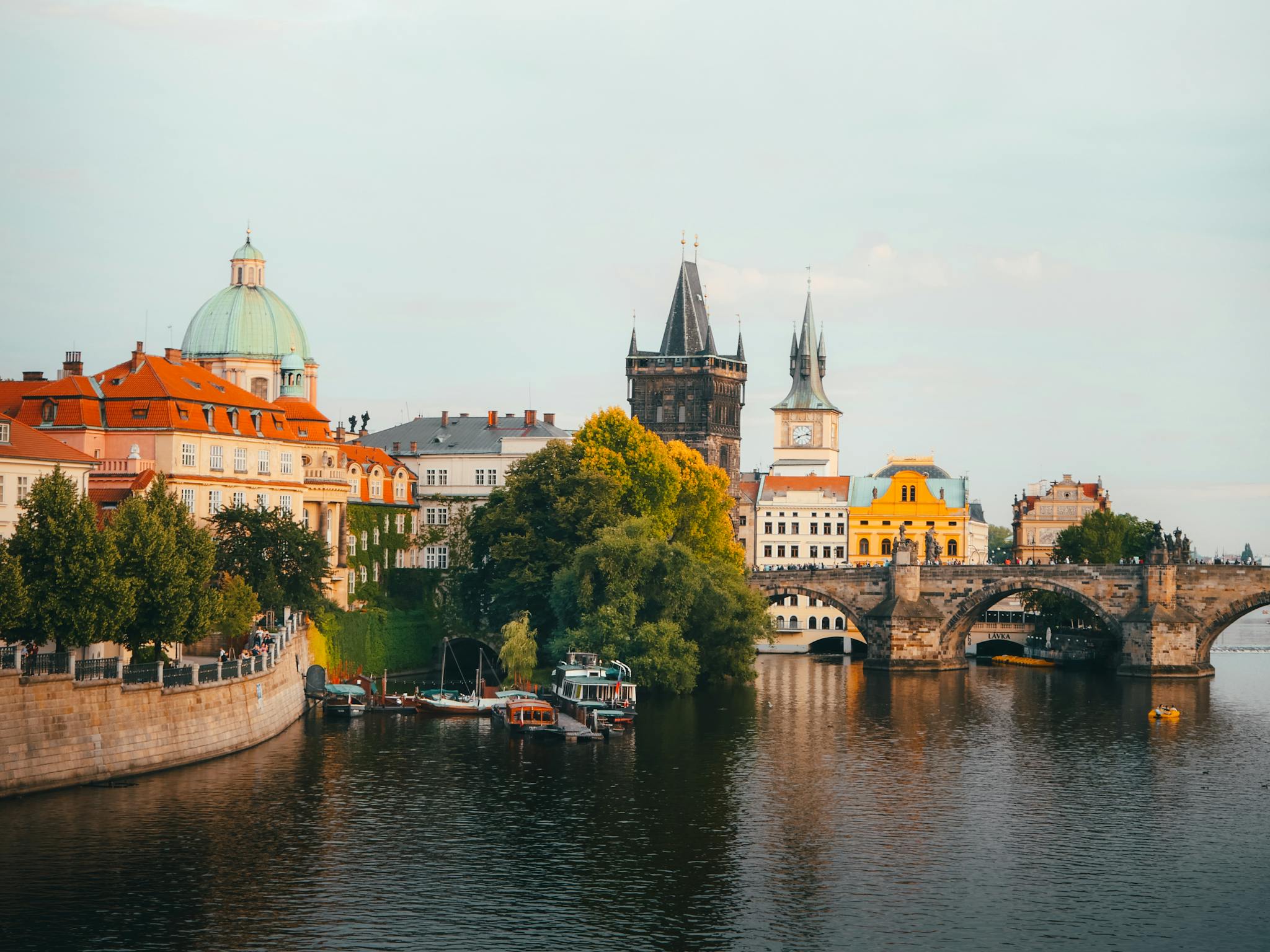 Scenic view of Charles Bridge and historical buildings of Prague at sunset with reflections in the river.
